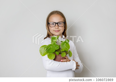 Beautiful clever kid girl in glasses with green plant in pot standing on white background. Beautiful clever kid girl in glasses with green plant in pot standing on white background. 106072869
