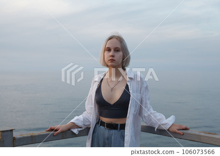 Portrait of  blonde woman in white shirt and tank top standing on pier 106073566