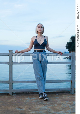 Blonde woman standing on pier on the background of blue sea and cloudy sky 106073568