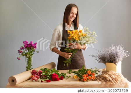 Skilled floral craftsmanship. Delicate flower compositions. Hard working woman florist creating beautiful bouquet at workplace in flower shop standing isolated over gray background 106073739