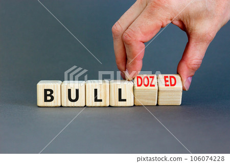 Bull or bulldozed symbol. Businessman turns wooden cubes and changes word Bull to Bulldozed. Beautiful grey table grey background. Business bull or bulldozed concept. Copy space. 106074228