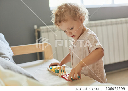 Enjoy leisure activities. Playful toddler imagination. Creative childhood development. Wavy haired blonde infant baby playing wooden educational toys at home interior. Enjoy leisure activities. Playful toddler imagination. Creative childhood development. Wavy haired blonde infant baby playing wooden educational toys at home interior. 106074299