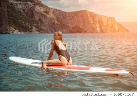Woman sup sea. Sports girl on a surfboard in the sea on a sunny summer day. In a black bathing suit, he sits on a sapa in the sea. Rest on the sea. Woman sup sea. Sports girl on a surfboard in the sea on a sunny summer day. In a black bathing suit, he sits on a sapa in the sea. Rest on the sea. 106075167