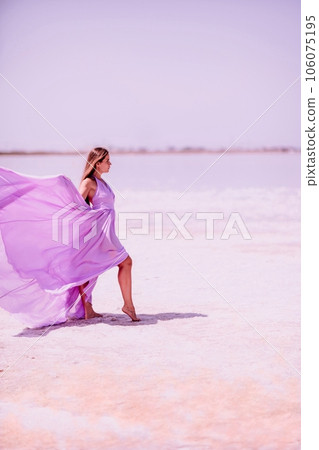 Woman pink salt lake. Against the backdrop of a pink salt lake, a woman in a long pink dress takes a leisurely stroll along the white, salty shore, capturing a wanderlust moment. 106075195