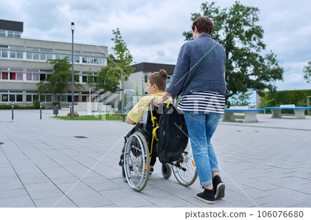 Back view of woman with disabled boy in wheelchair near school building 106076680