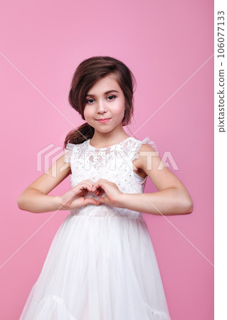 Adorable little girl showing heart gesture with hands on pink studio background 106077133