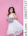 Smiling kid girl in birthday party princess hat holding gift box on a pink background. Kid birthday 106077137