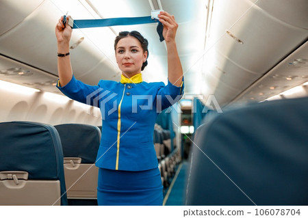 Female flight attendant with seatbelt standing in aircraft cabin 106078704