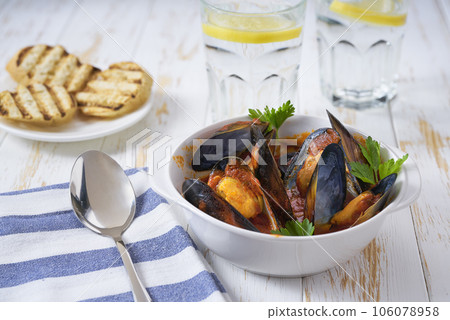 mussels cooked in a tomato sauce on a white wooden table. 106078958