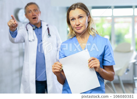 Upset middle-aged nurse standing with her back to angry doctor Upset middle-aged nurse standing with her back to angry doctor 106080381