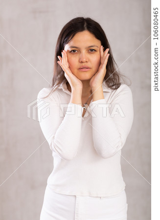 Young female model arbitrarily holds hands at face,one above other. 106080465