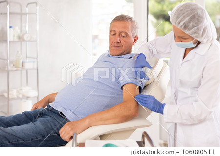 Old man patient having arm injection lying on clinical chair 106080511