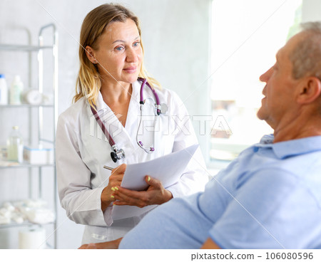 Middle-aged female doctor signing papers while talking with man patient Middle-aged female doctor signing papers while talking with man patient 106080596