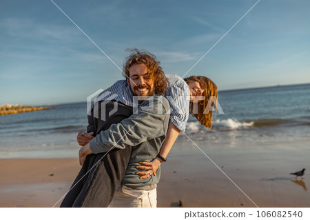 Smilng couple in love fool around while walking along the beach on sunny windy day 106082540
