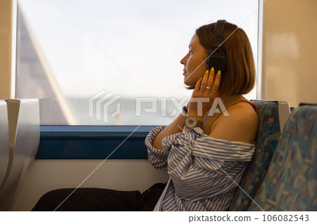 Woman in headphones while traveling in public transport and looking view outside the window 106082543