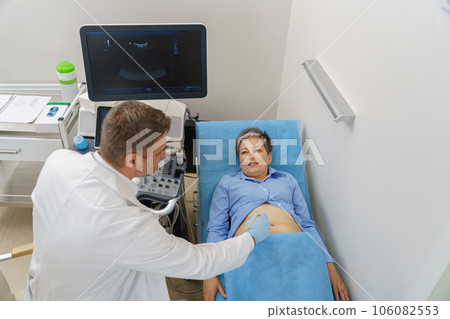 Middle aged woman patient lying on bed and having ultrasound examination of abdomen in clinic Middle aged woman patient lying on bed and having ultrasound examination of abdomen in clinic 106082553