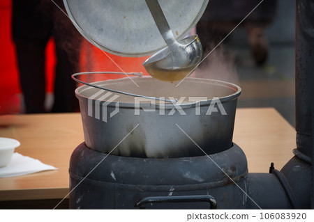 Outdoor preparing soup in a cast iron boiler 106083920