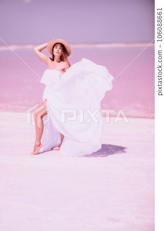 Woman in pink salt lake. She in a white dress and hat enjoys the scenic view of a pink salt lake as she walks along the white, salty shore, creating a lasting memory. Woman in pink salt lake. She in a white dress and hat enjoys the scenic view of a pink salt lake as she walks along the white, salty shore, creating a lasting memory. 106088661