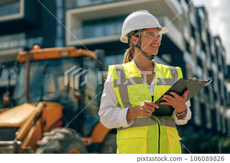 Professional female engineer in protective helmet making notes on construction site 106089826