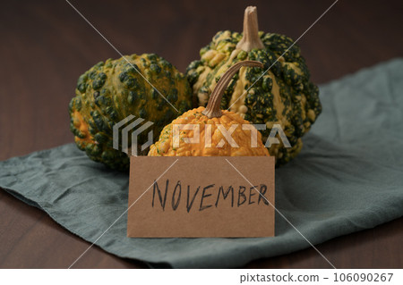 decorative pumpkins on walnut wood table with november paper card 106090267