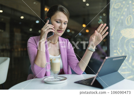 Young business woman solves business issues remotely by phone while sitting in a cafe Young business woman solves business issues remotely by phone while sitting in a cafe 106090473