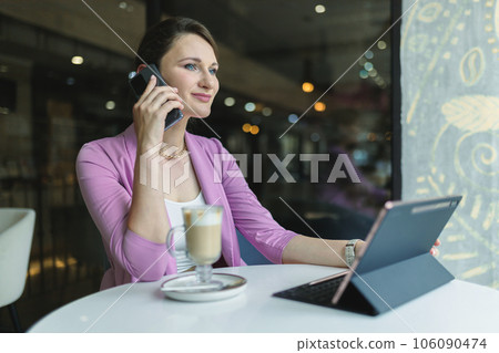 Attractive caucasian female freelancer talking on mobile phone while working in cafe behind laptop Attractive caucasian female freelancer talking on mobile phone while working in cafe behind laptop 106090474