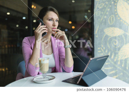A young businesswoman seriously and thoughtfully speaks on the phone in a cafe, discusses important matters of the company A young businesswoman seriously and thoughtfully speaks on the phone in a cafe, discusses important matters of the company 106090476