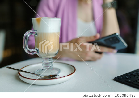 Business woman sitting in cafe with a laptop and smartphone, In the foreground, a tall glass with latte coffee close-up Business woman sitting in cafe with a laptop and smartphone, In the foreground, a tall glass with latte coffee close-up 106090483