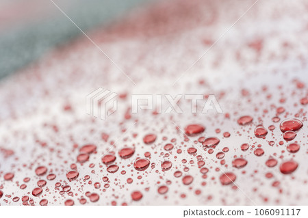 Rain droplets on red sports car surface with hydrophobic treatment 106091117
