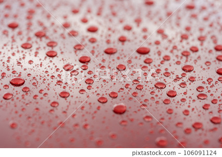 Rain droplets on red sports car surface with hydrophobic treatment 106091124