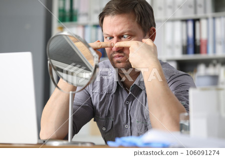 Portrait of middle-aged man sitting opposite small table mirror and squeezing acne problems Portrait of middle-aged man sitting opposite small table mirror and squeezing acne problems 106091274