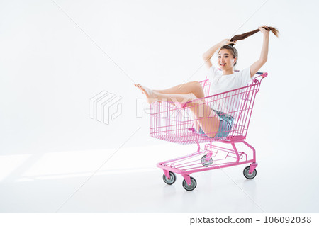 Carefree shopaholic girl rides in a shopping cart and enjoys sales on white background with copy space. 106092038