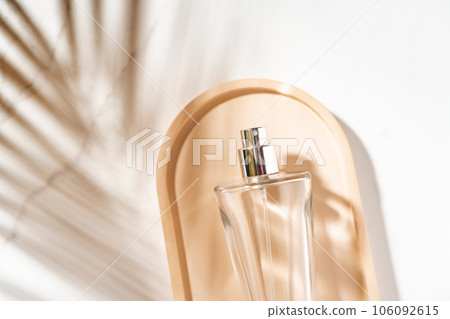 Perfumery summer fragrance background with glass perfume bottle on the tray with palm leaves shadow on the table Perfumery summer fragrance background with glass perfume bottle on the tray with palm leaves shadow on the table 106092615