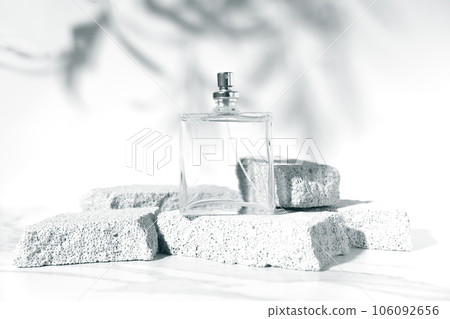 Summer fragrance concept with mockup transparent perfume bottle standing on pumice stones on white background with shade of leaves. Studio photography. 106092656