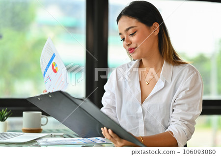 Attractive female manager reading paper document, analyzing marketing data, statistics, financial results at office desk Attractive female manager reading paper document, analyzing marketing data, statistics, financial results at office desk 106093080