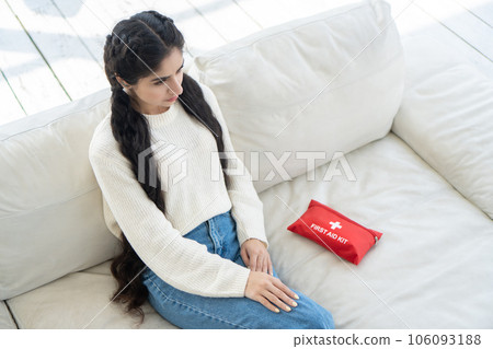 Young woman with health problem about her physical condition sits on the couch next to her home first aid kit. Unwanted pregnancy and malaise concept. 106093188