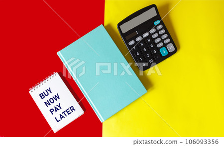 Notepad with the words BUY NOW PAY LATER on a red and yellow background with a green diary Notepad with the words BUY NOW PAY LATER on a red and yellow background with a green diary 106093356