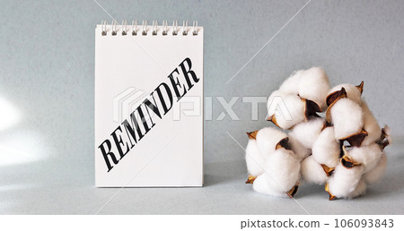 Reminder, the word is written on a notebook, a branch of cotton lies on a blue background 106093843