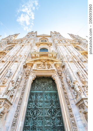 Milan Cathedral, Italian: Duomo di Milano, or Metropolitan Cathedral-Basilica of the Nativity of Saint Mary. View of main door and white marble facade on sunny summer day. Milan, Lombardy, Italy 106093960