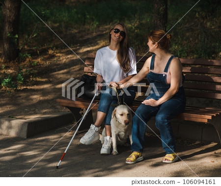 Blind caucasian woman sitting on bench with guide dog and pregnant friend. Blind caucasian woman sitting on bench with guide dog and pregnant friend. 106094161