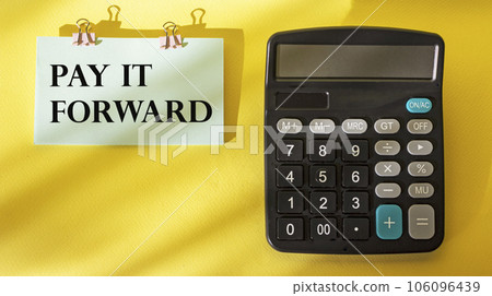 Phrase Pay It Forward text on white sticker posted on yellow background with calculator Phrase Pay It Forward text on white sticker posted on yellow background with calculator 106096439
