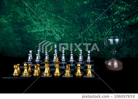 Chess Board and Chess Pieces with Hourglass on a Wooden Table with Mottled Background 106097659