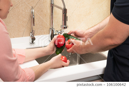 happy couple washes vegetables for lunch in their hands in the kitchen in the sink close-up 106100642