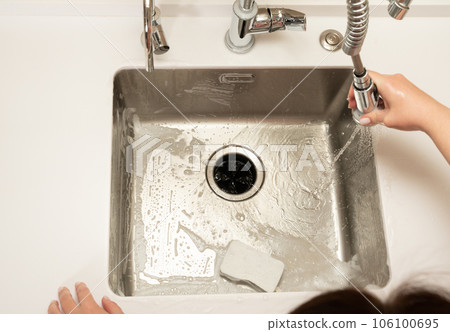 the girl washes away the foam in the kitchen sink from the sprayer faucet 106100695