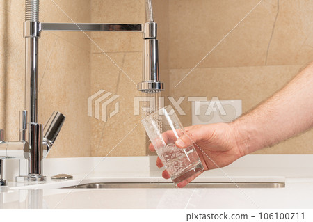 man picking up a glass of drinking water in the kitchen man picking up a glass of drinking water in the kitchen 106100711