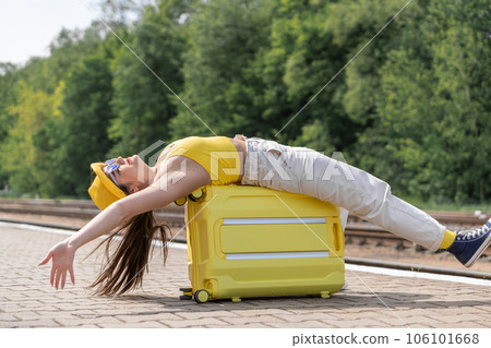 Kiss of the wind: a traveler in a yellow coat is ready to relax in the open air. A woman is lying on her suitcase, waiting for transport or has just arrived at the scene 106101668