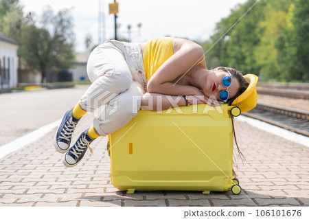 The woman lay down on her suitcase and waited in stylish yellow clothes and blue glasses for a real traveler, ready to discover new places on vacation. 106101676