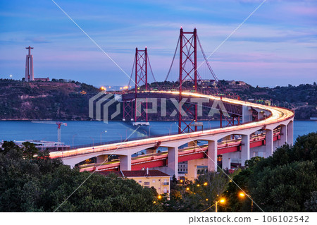 View of Lisbon view from Miradouro do Bairro do Alvito viewpoint of Tagus river, traffic with light trails on 25th of April Bridge, and Christ the King statue in the evening twilight. Lisbon, Portugal View of Lisbon view from Miradouro do Bairro do Alvito viewpoint of Tagus river, traffic with light trails on 25th of April Bridge, and Christ the King statue in the evening twilight. Lisbon, Portugal 106102542