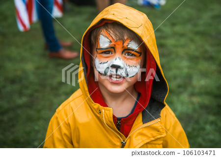 cute little boy with colorful painted face like tiger. funny face. child in the yellow raincoat. cute little boy with colorful painted face like tiger. funny face. child in the yellow raincoat. 106103471