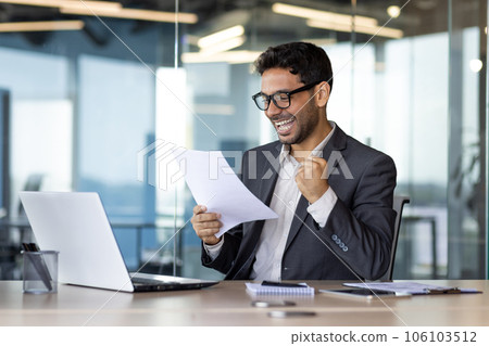 Arab investor financier, holding hand up winner triumphant gesture, businessman at workplace inside office paper work, looking at reports, satisfied with results of financial success achievement. 106103512
